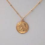 Closeup on coin design of the angel baby coin necklace.  Angel is depicted from the chest up and is resting his chin in one hand.