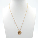 A sleek, modern gold chain with a coin pendant on it that has a design of angel wings seen from the back.